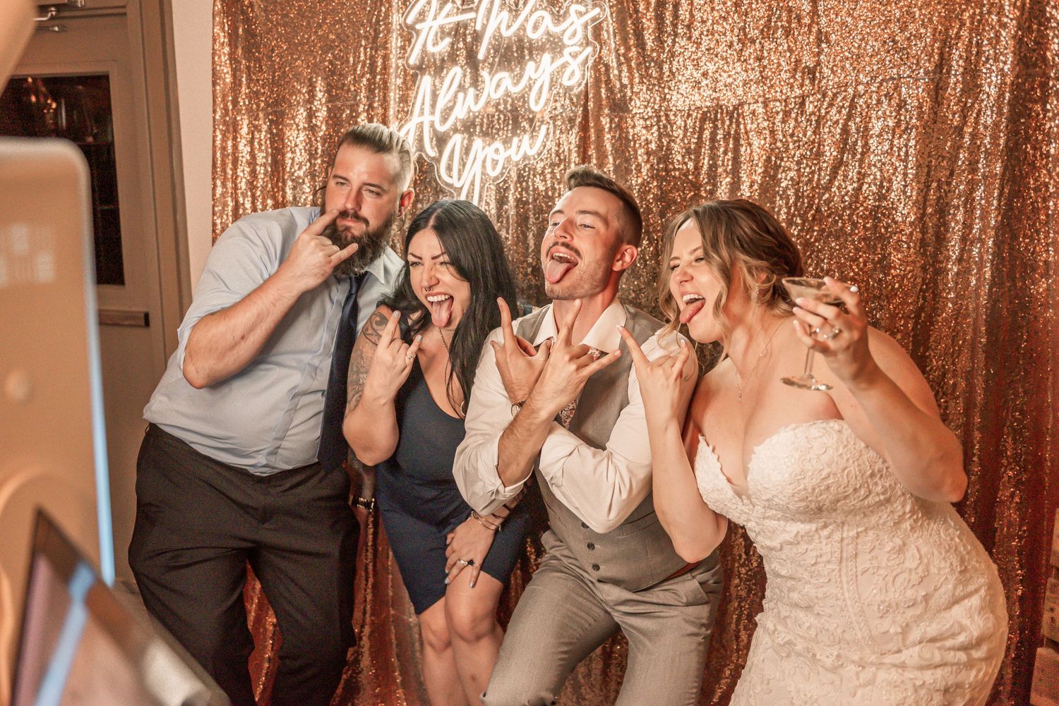 Wedding reception guests having fun and dancing in front of a rose gold sequin backdrop.