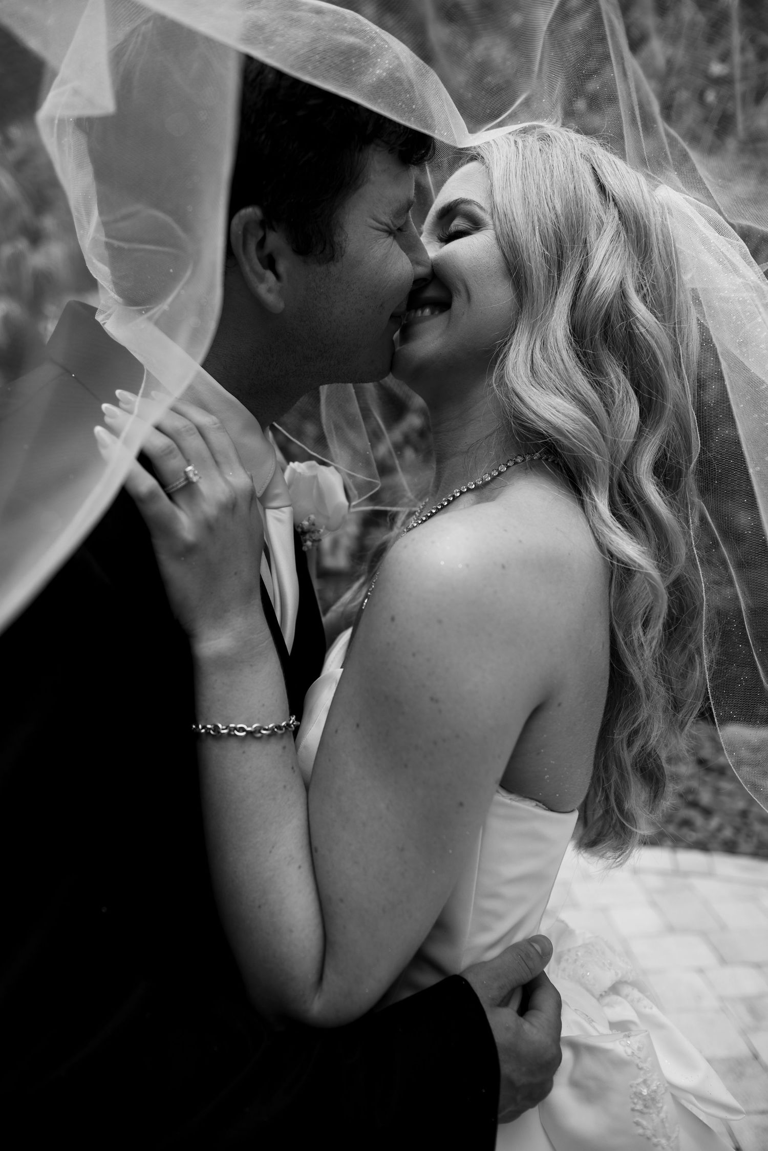 Black and white wedding photo of bride and groom sharing a romantic kiss under a flowing veil.