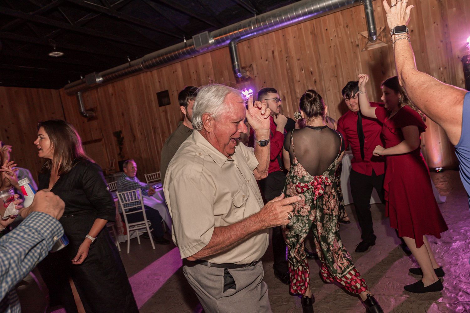 People dancing together at a rustic barn venue with pink lighting and wooden walls.