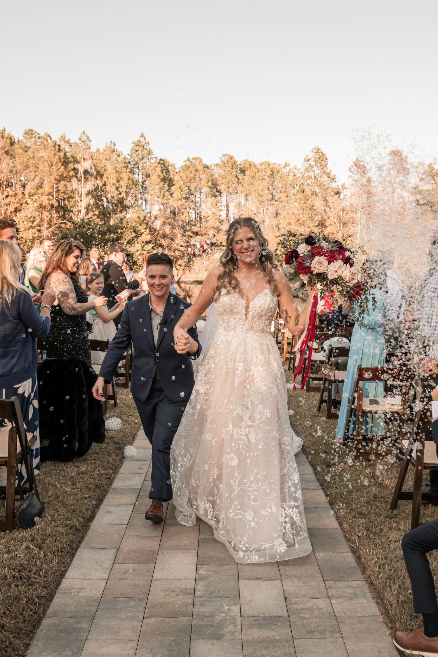 Wedding couple walks down aisle while guests throw confetti during recessional at outdoor autumn ceremony.
