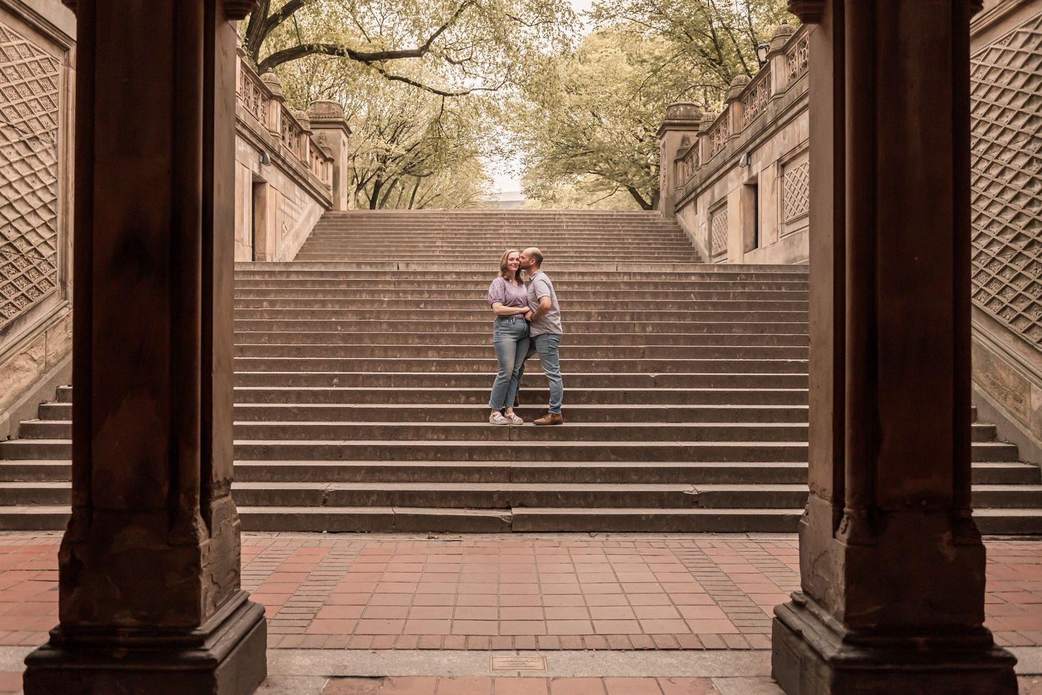 A couple sits together on grand stone stairs at Bethesda Terrace in New York's Central Park on an autumn afternoon.