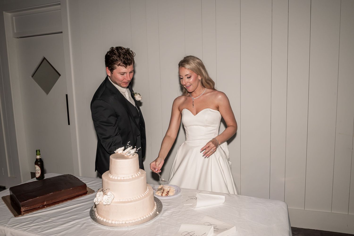 Bride and groom cutting their white wedding cake together at the reception table.