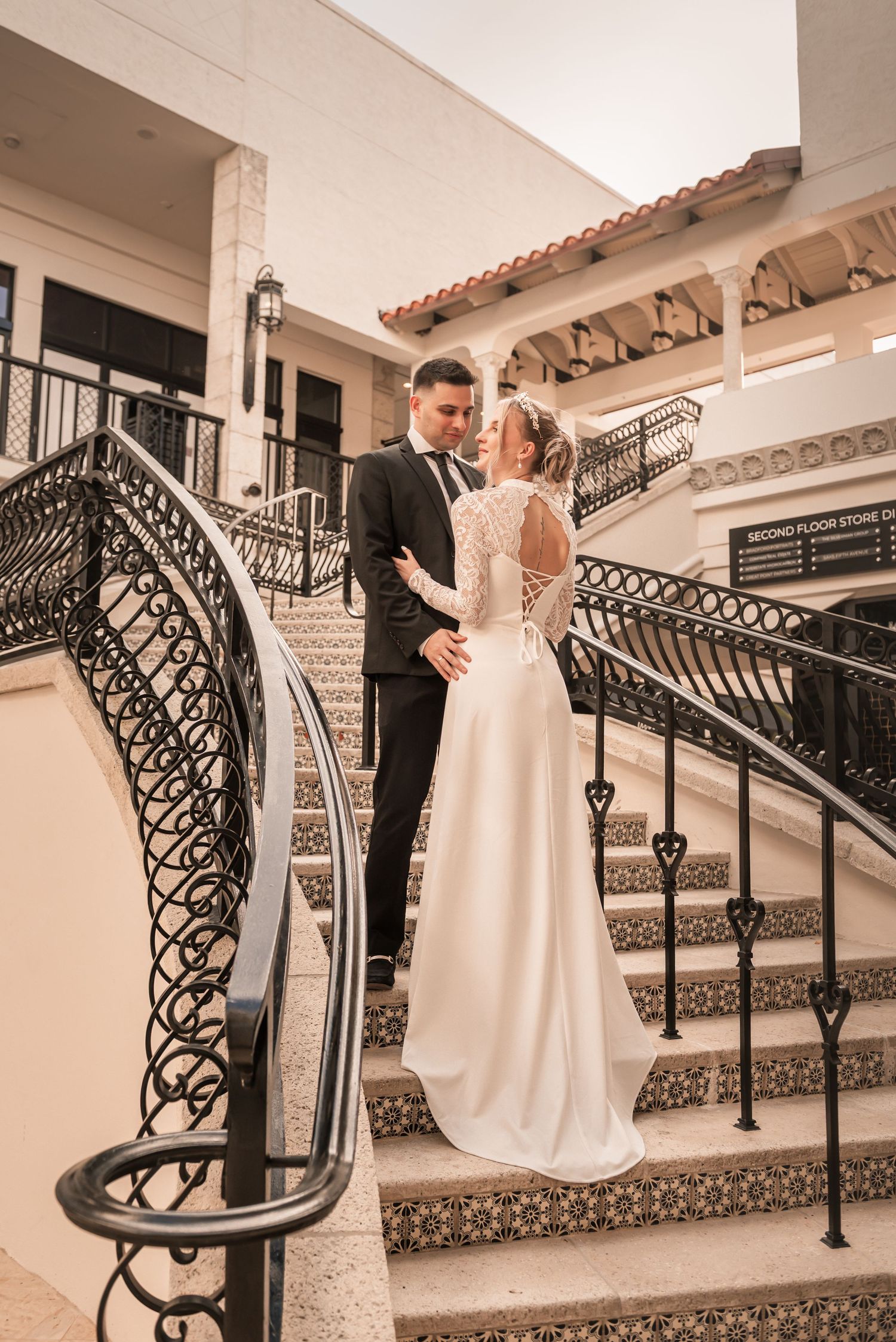Bride and groom share a romantic moment on ornate staircase steps at elegant wedding venue.