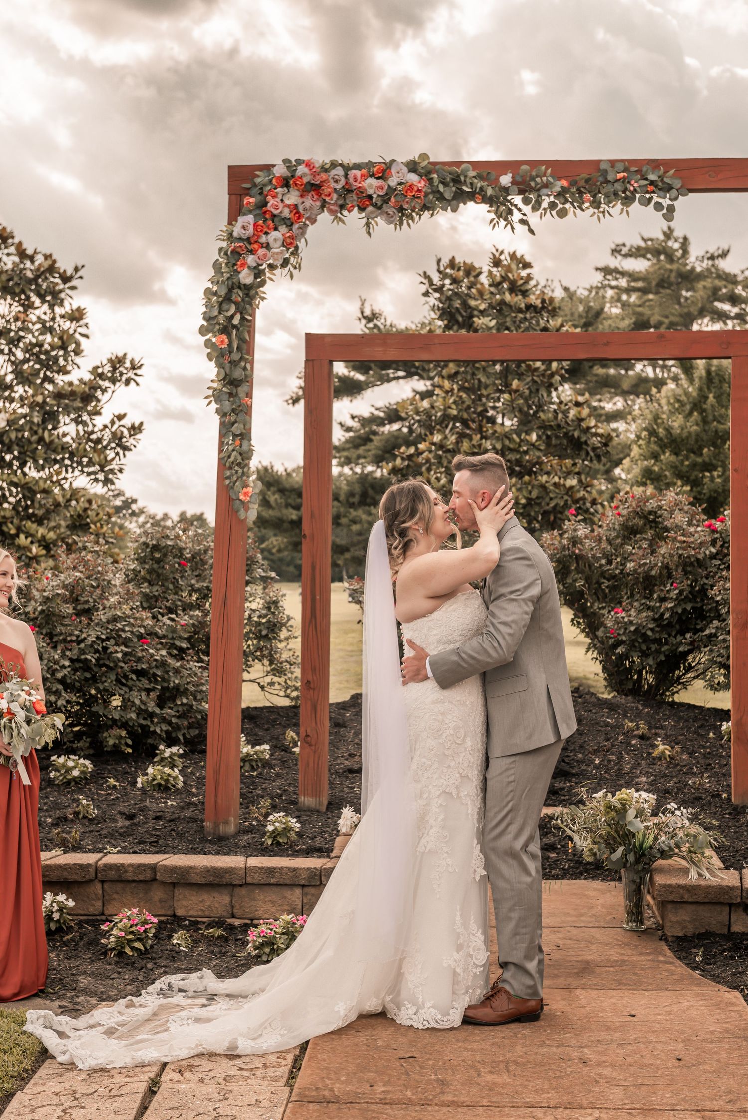 Wedding couple shares intimate moments underneath red wooden pergola structures in garden setting.