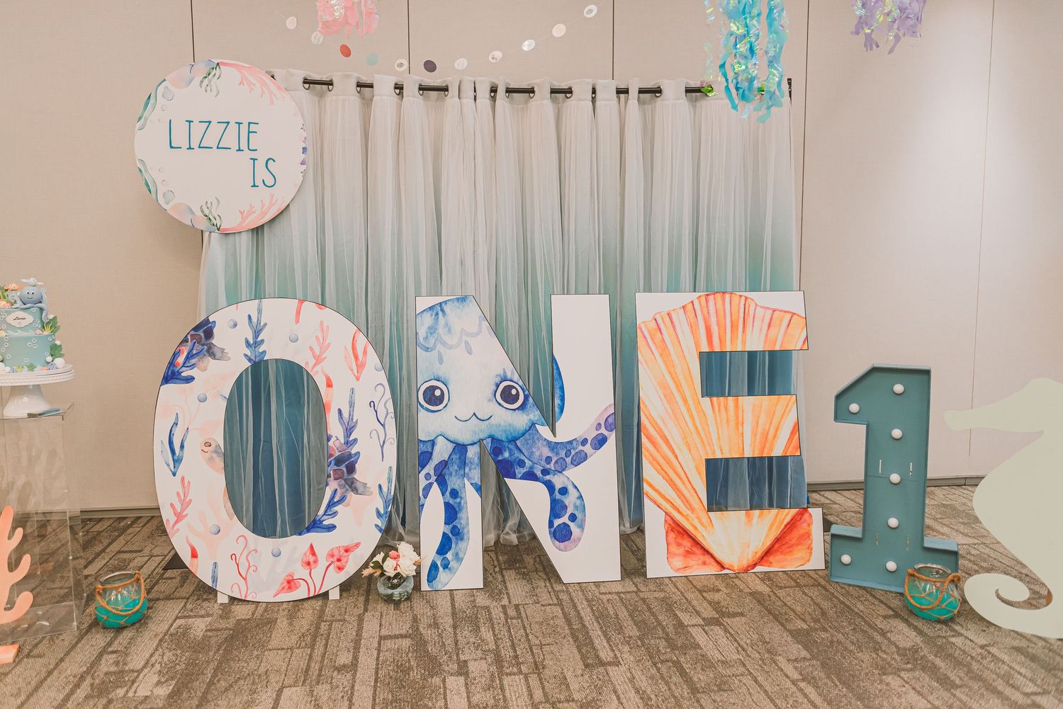 Decorative oversized letters spelling ONE with blue and coral colors in a whimsical birthday party setting.