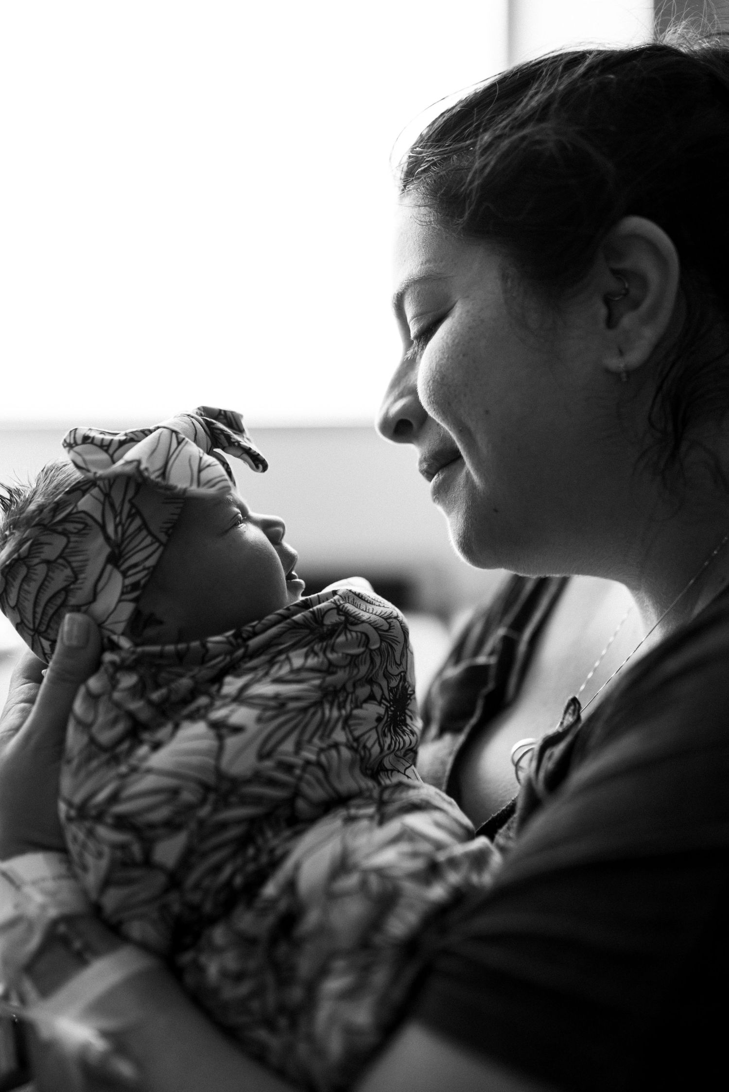 Black and white photo of a smiling mother tenderly holding her newborn baby wrapped in a floral blanket.