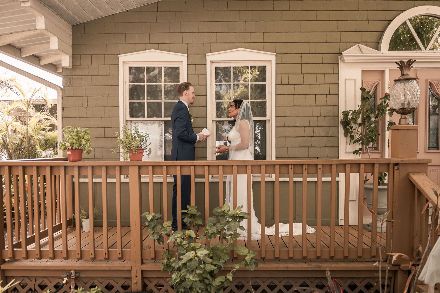 Bride and groom sharing a moment on a wooden porch of a green house.