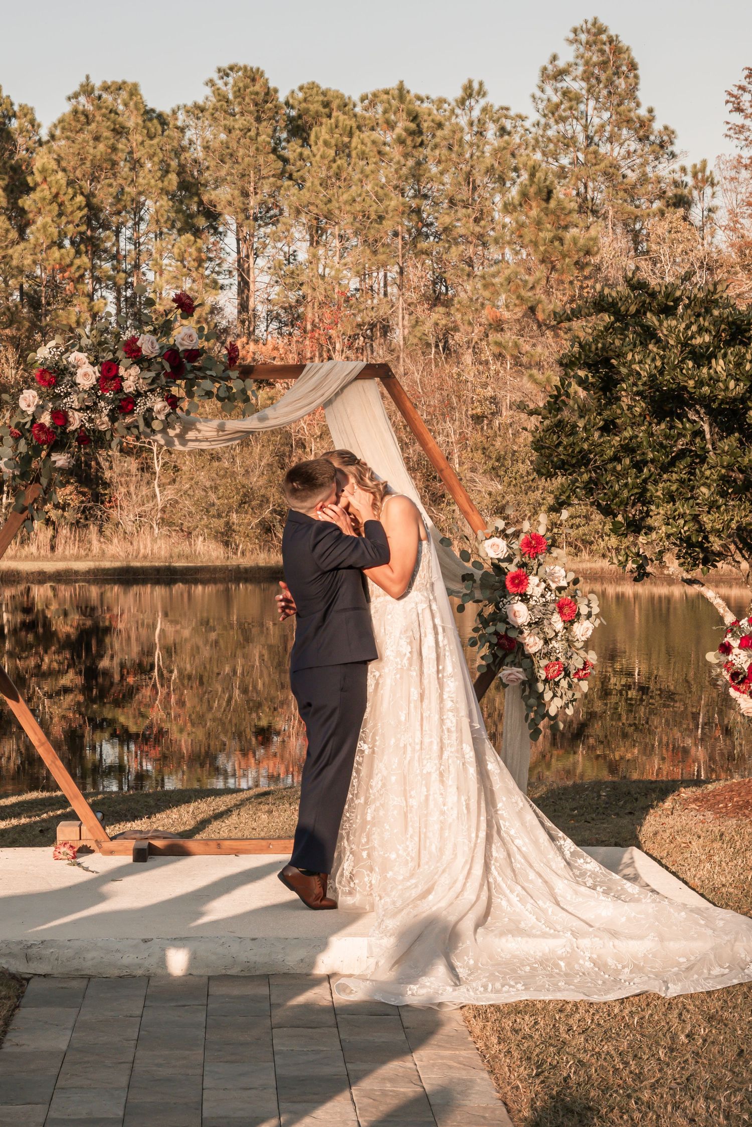 A romantic outdoor wedding ceremony by a serene lake with floral arrangements and autumn trees in the background.