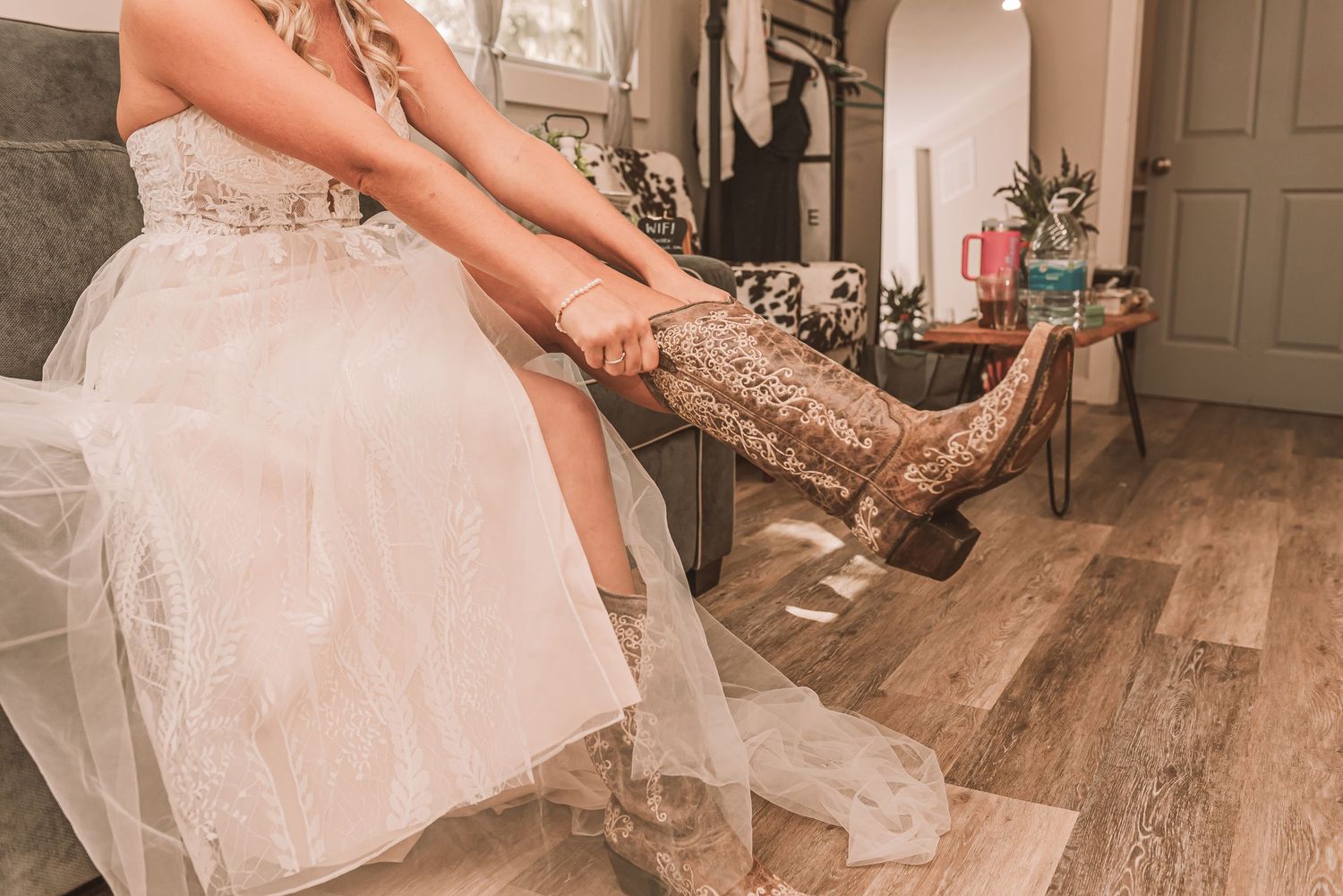 A person in a tulle wedding dress puts on sparkly gold boots while sitting on a rustic wooden floor.
