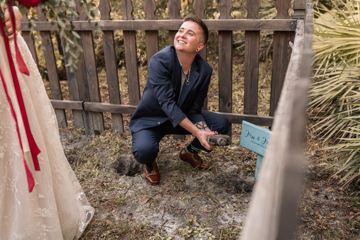A person in a navy coat sits on a wooden bench in an outdoor garden setting with rustic fencing.