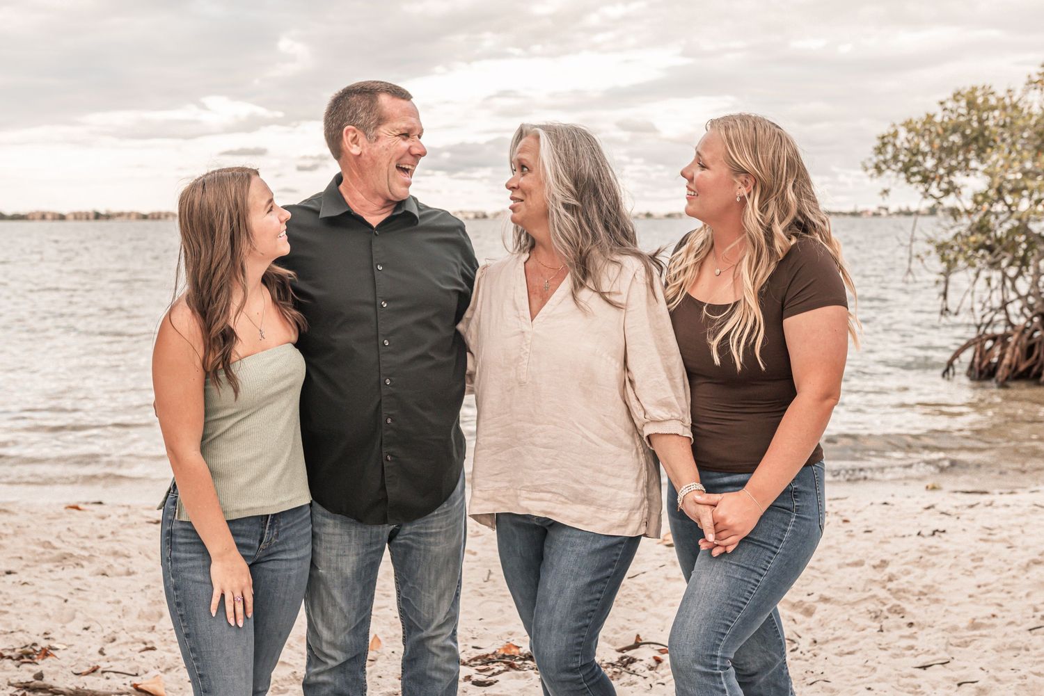A family laughs together while walking along a sandy beach at sunset.