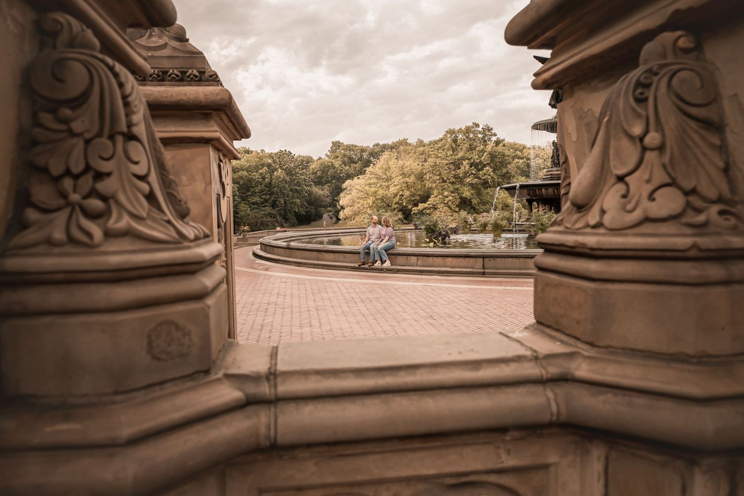 View through ornate stone columns of Bethesda Terrace in Central Park with people sitting on steps in warm autumn light.