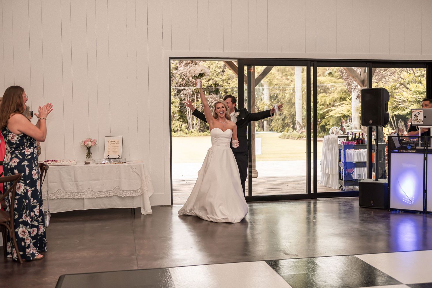 Bride and groom share first dance at wedding reception on checkered dance floor with guests applauding nearby.