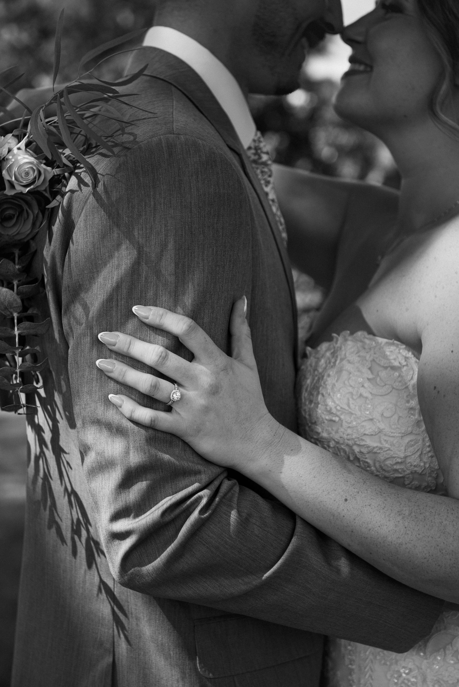 A tender black and white wedding moment showing a bride's hand with ring resting on her groom's suit jacket.