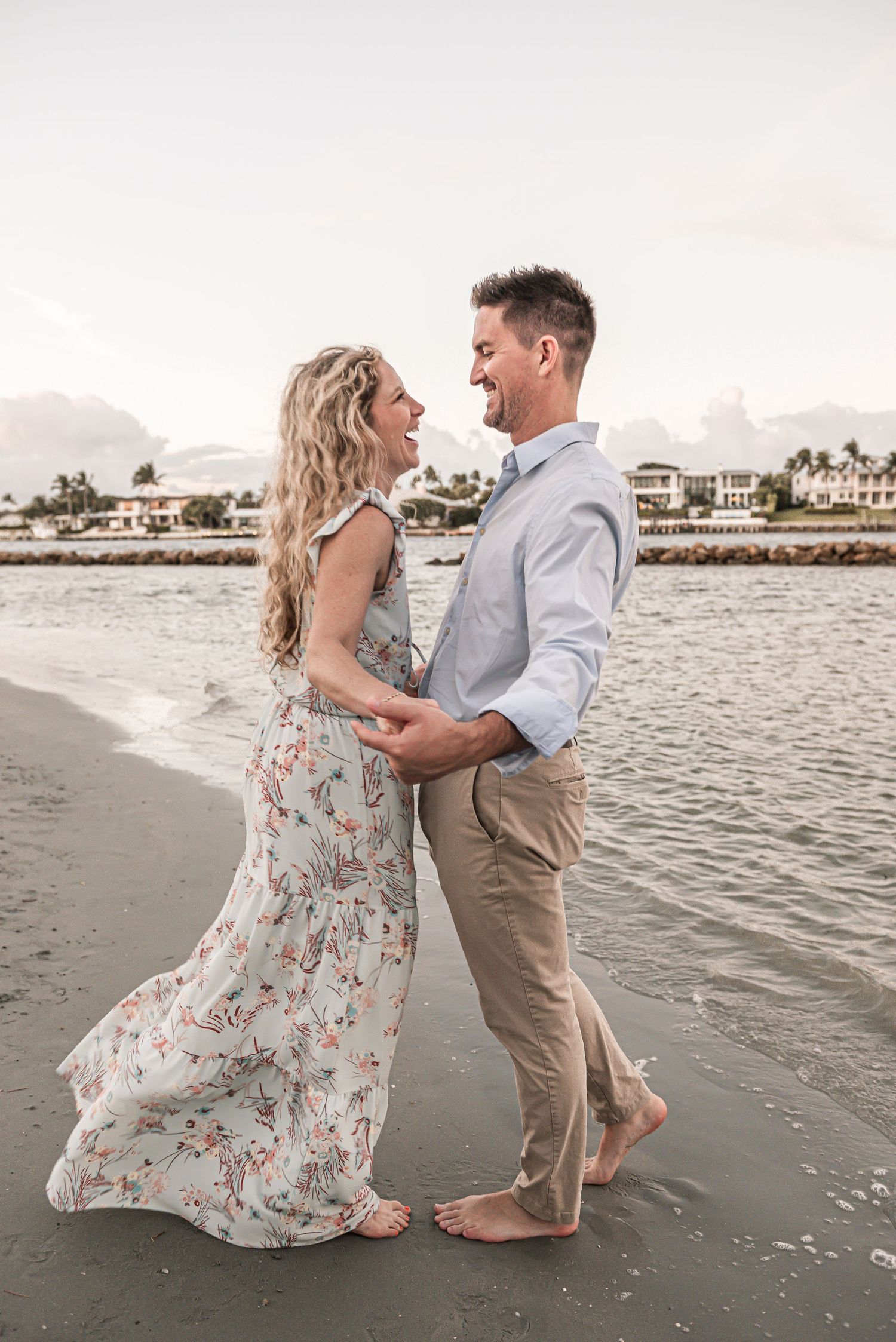 Couple dancing together on a beach at sunset as flowy floral dress catches the ocean breeze.