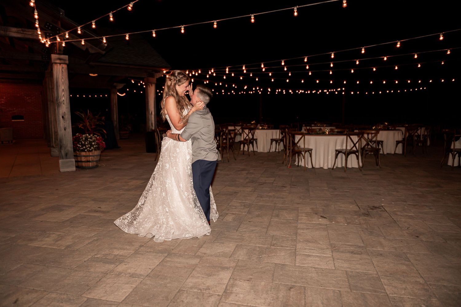 A couple shares their first dance at a rustic barn wedding reception under romantic string lights.