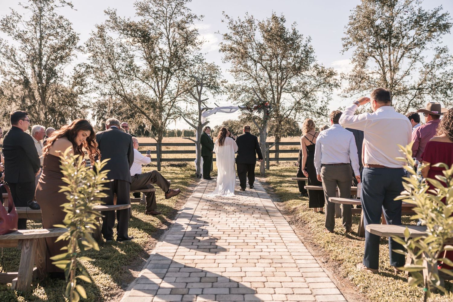 A panoramic sequence of an outdoor wedding ceremony with guests gathered on a sunny day in a natural setting.