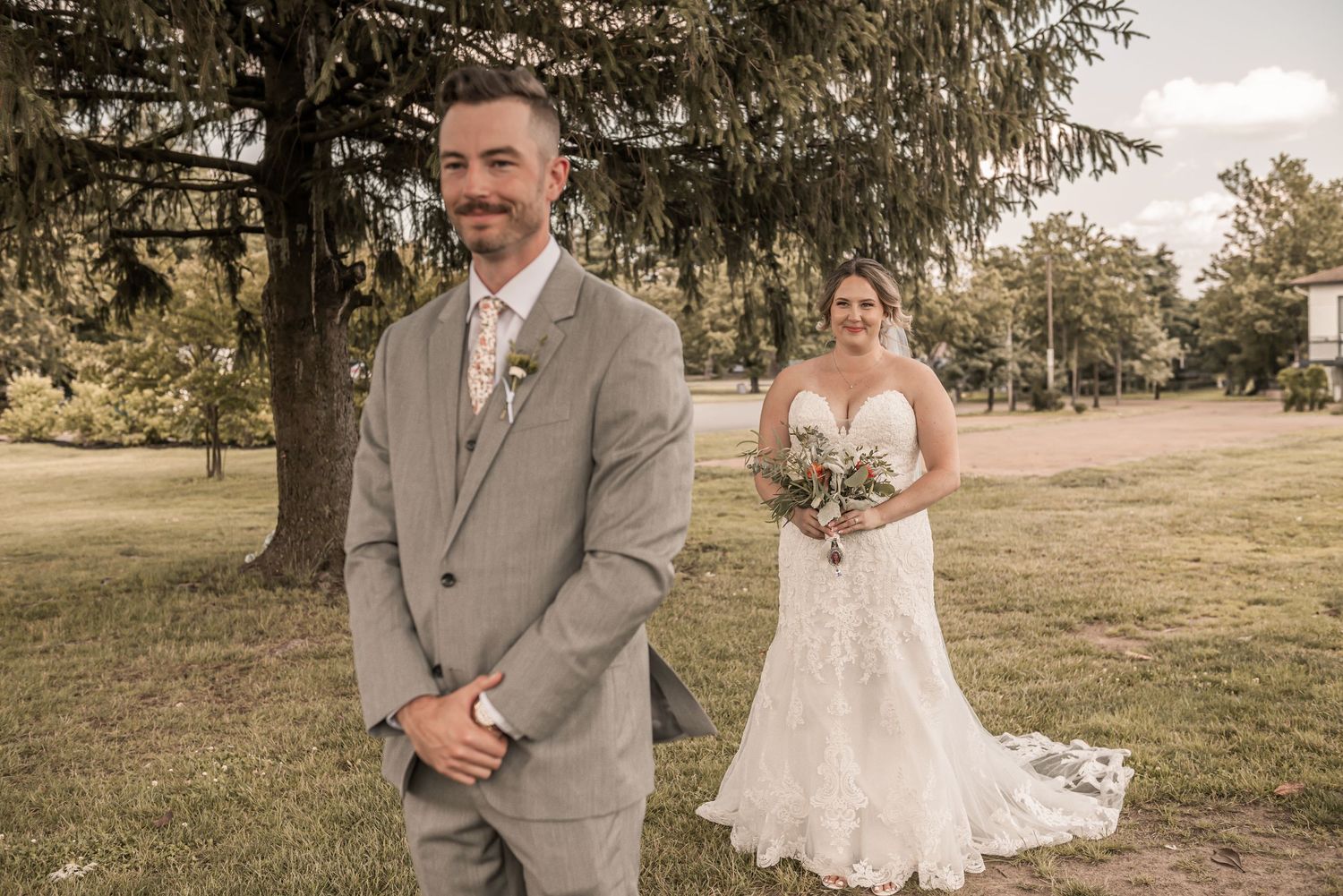 A wedding party walks through a scenic outdoor venue with tall evergreen trees in the background.
