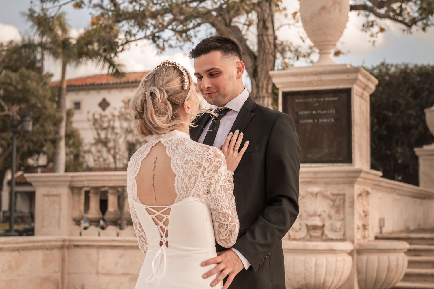 Bride and groom share a romantic moment in front of a fountain, bride wearing a lace back wedding gown.
