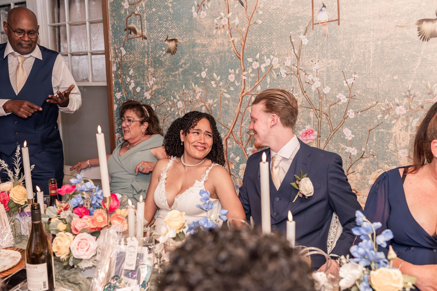 Bride and groom smiling at wedding reception table with floral centerpieces and candles.