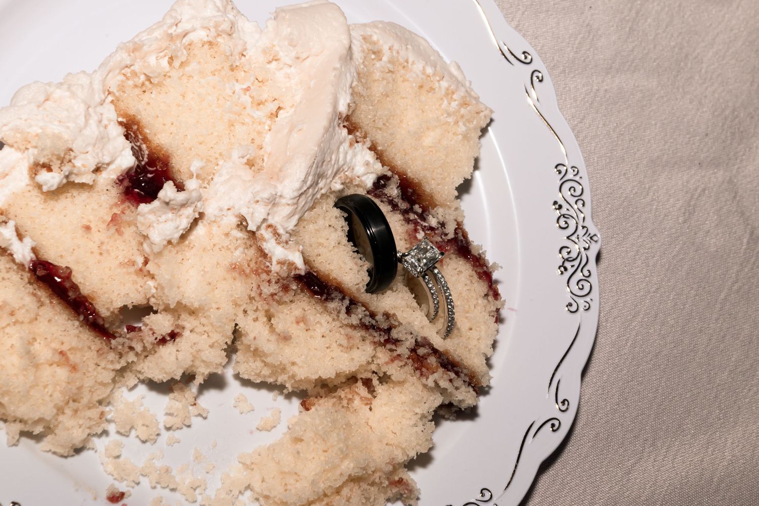 Wedding rings placed on a slice of white cake with raspberry filling on an elegant decorative plate.