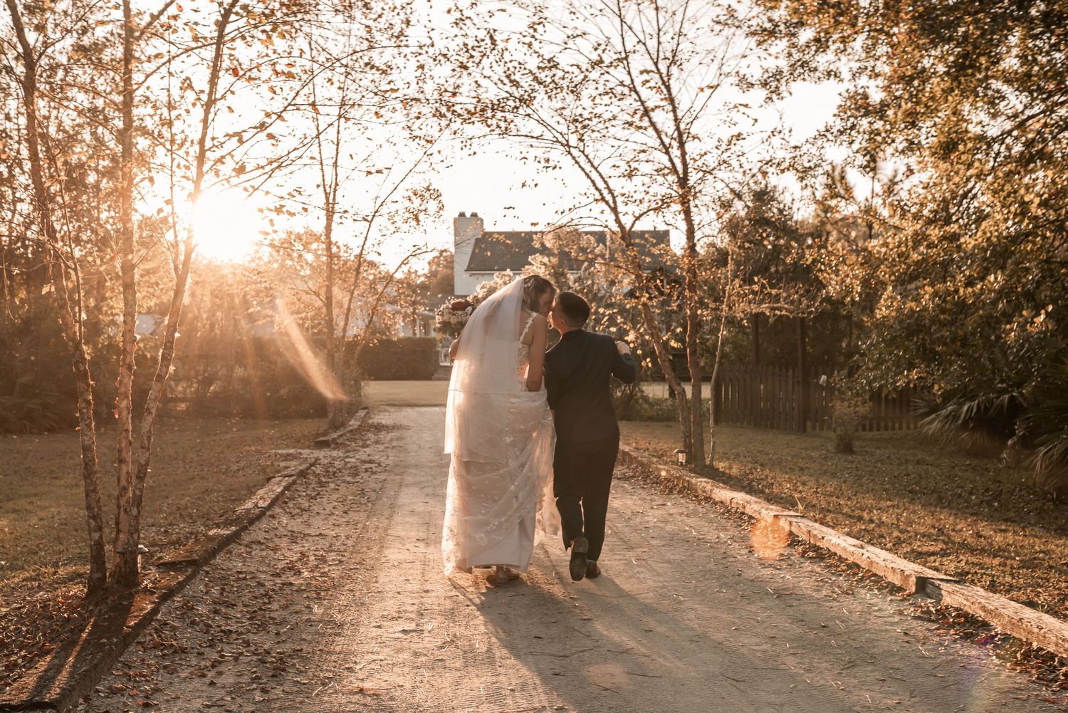 Silhouetted couple walks hand in hand along a sunlit autumn path with golden light streaming through trees.