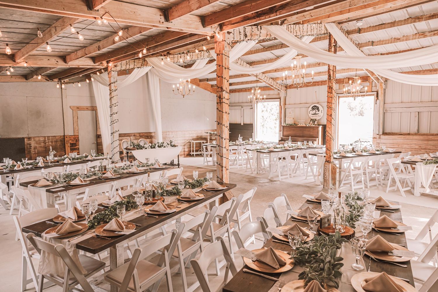 Rustic barn wedding reception venue with exposed wooden beams and elegant table settings in warm lighting.