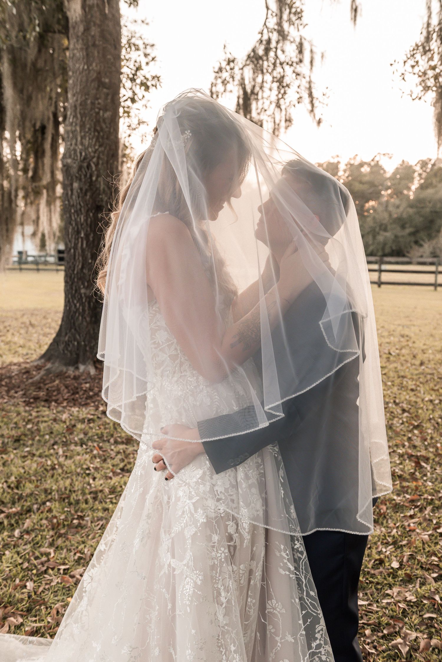 A romantic first look wedding moment captured through a bride's flowing veil under Spanish moss trees.