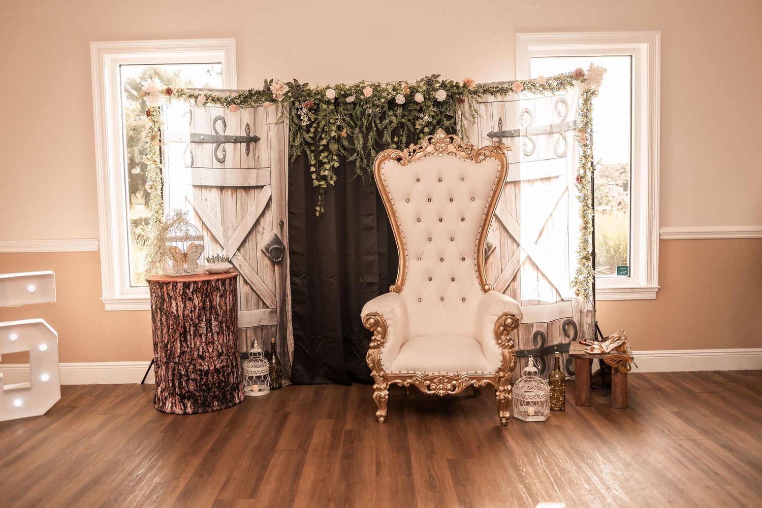 Elegant throne chair with tufted ivory upholstery displayed between rustic barn doors with floral greenery decor.