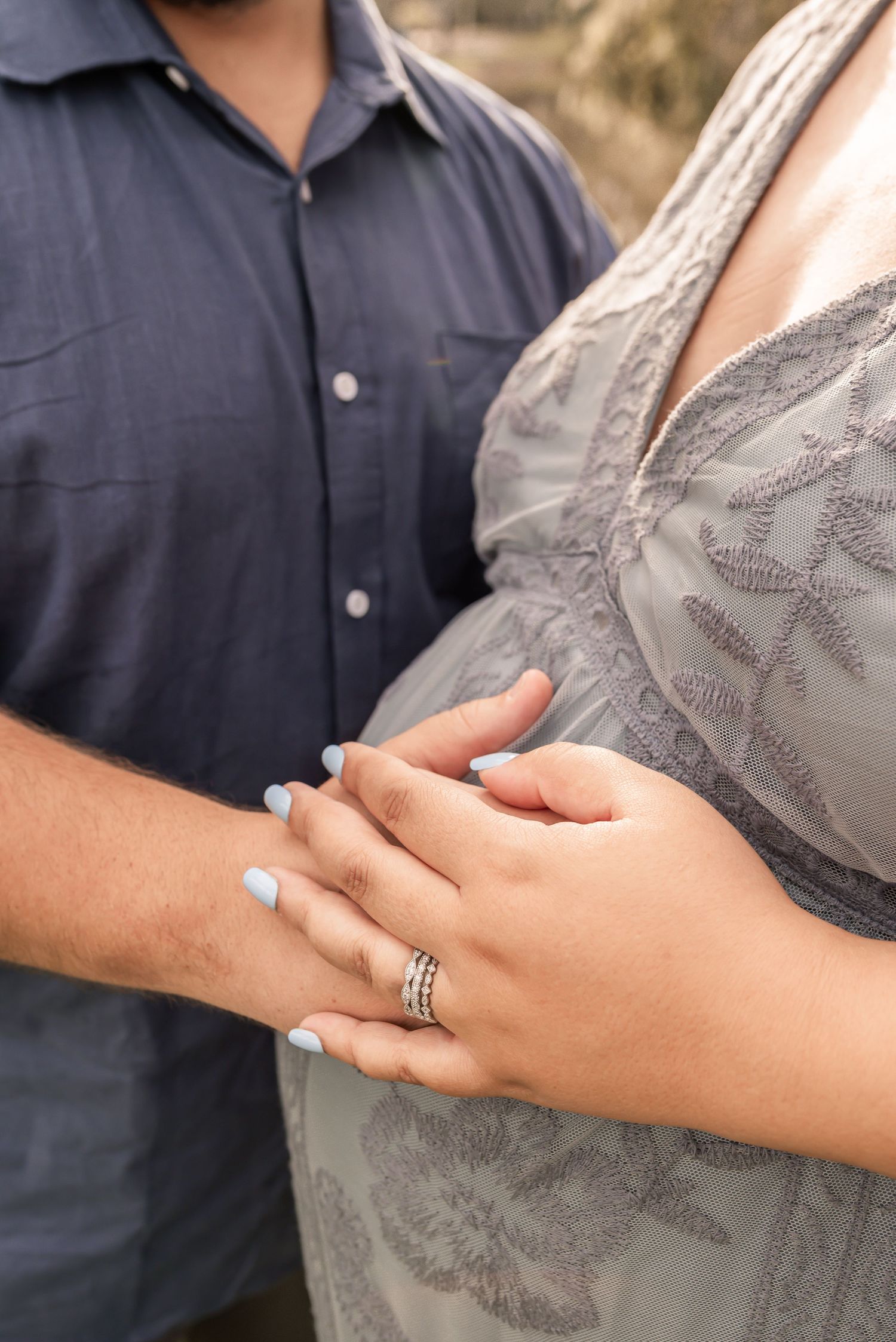 Close up of hands clasped together showing engagement or wedding ring with blue shirt and lace dress visible.