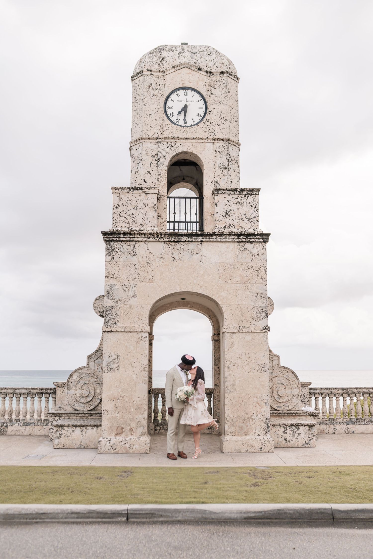 A couple poses beneath a historic clock tower archway with ornate stone architecture.