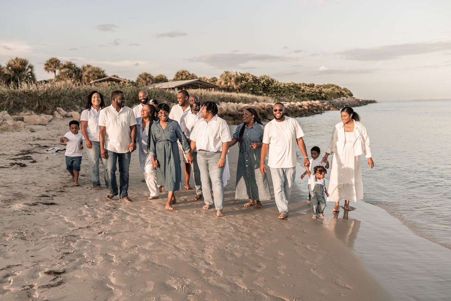 People gathered on sandy beach during golden hour with waves and coastline visible in distance.
