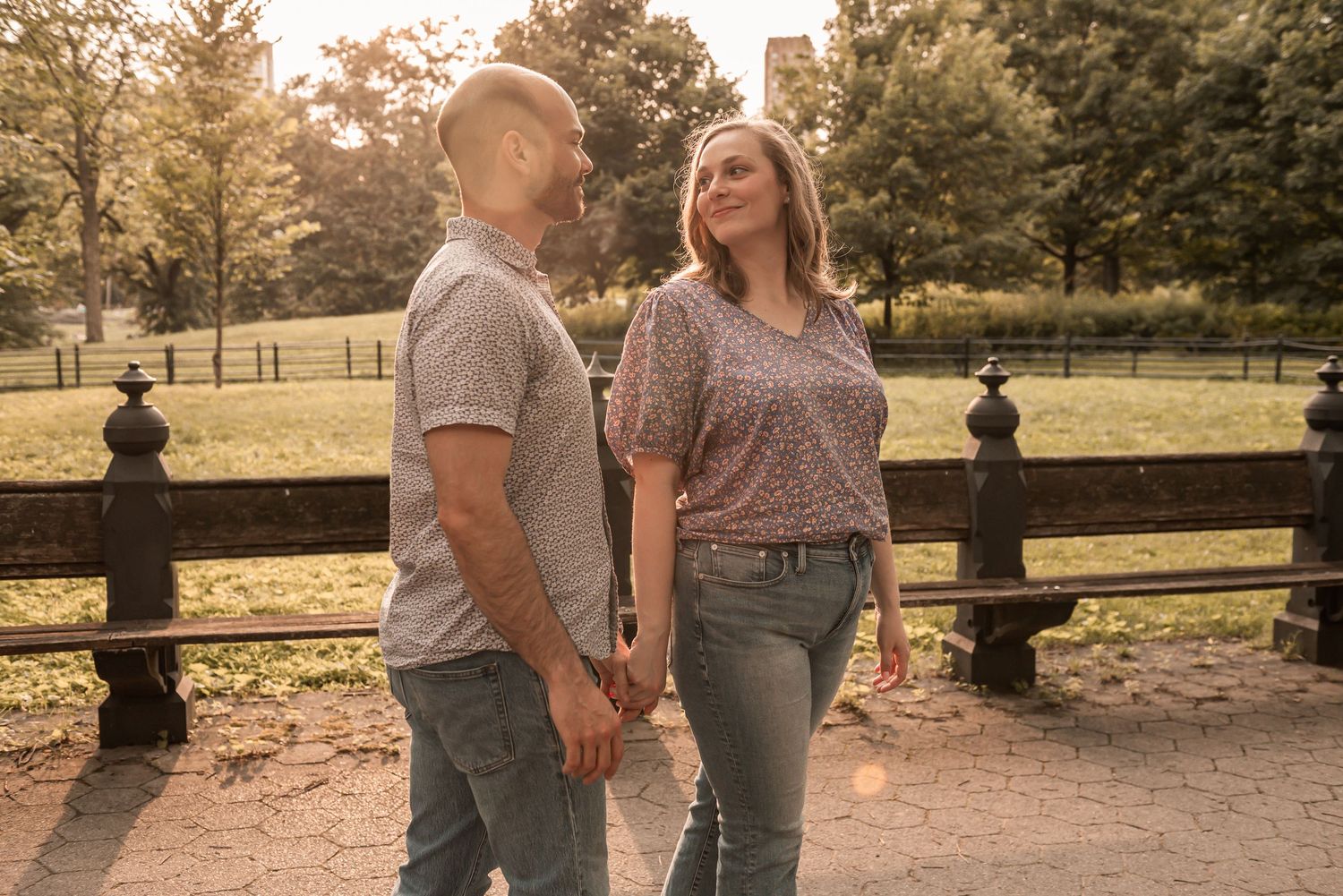 Two people in casual wear hold hands while walking through a scenic park at sunset.