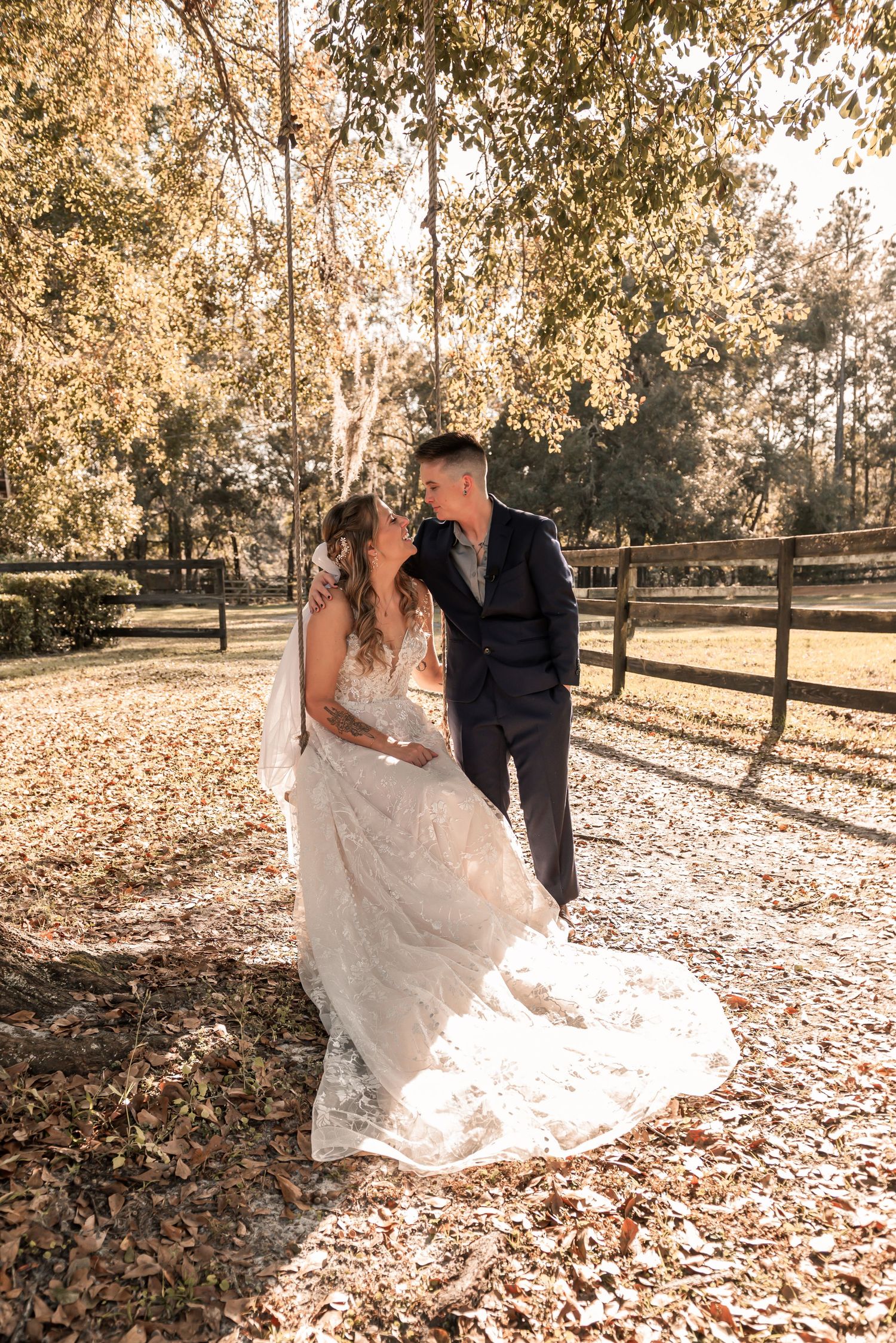 A couple in wedding attire dance together in a park with autumn leaves scattered on the ground during golden hour.
