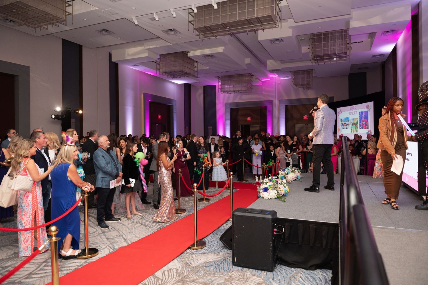 A panoramic view of a formal event with a red carpet walkway and purple lighting illuminating the space.