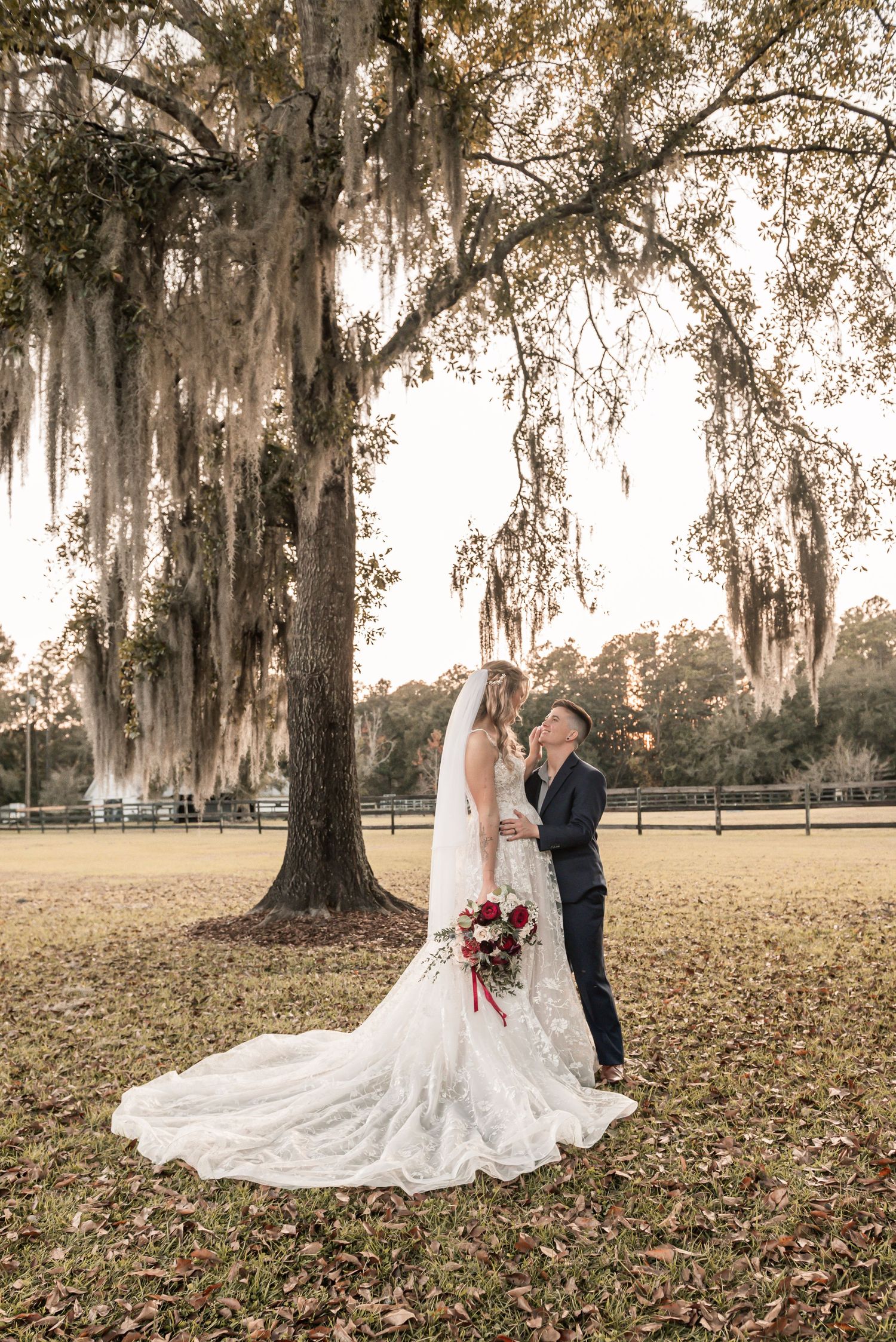 Romantic autumn wedding photos under Spanish moss draped oak trees with bride's flowing white dress trailing on fallen leaves.