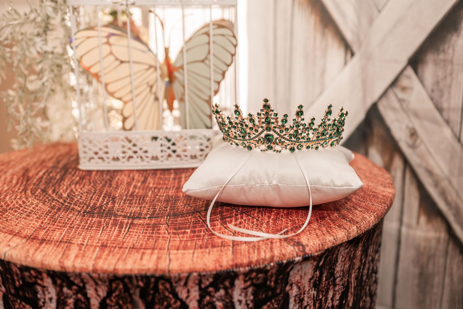 Gold crown with red gems resting on a white satin pillow atop a rustic wood stump at a fairy-tale wedding.