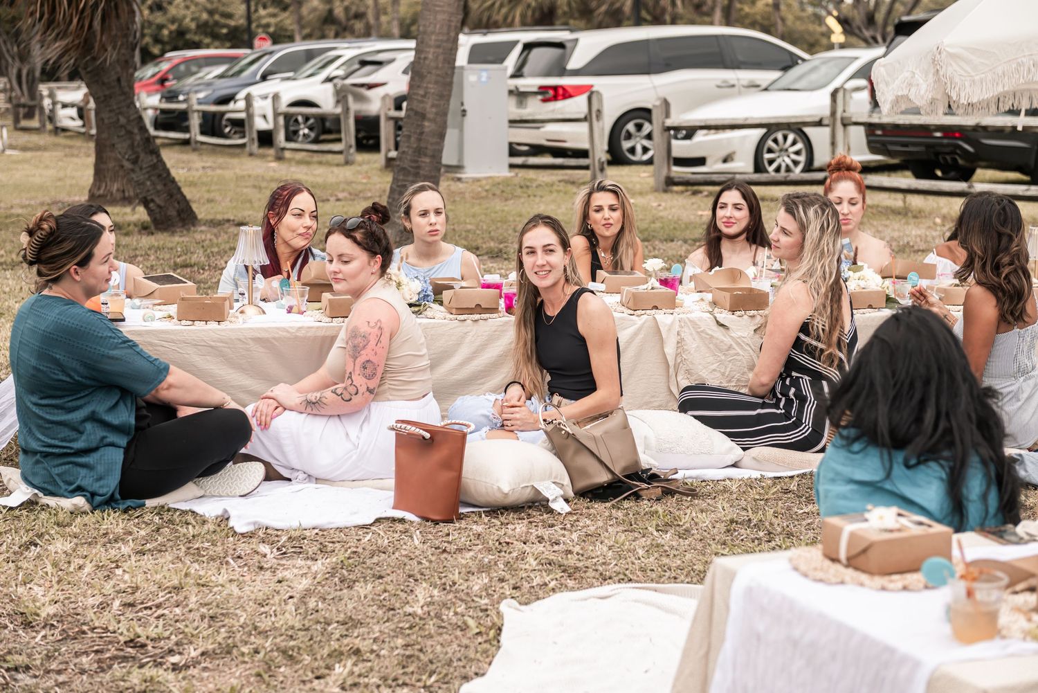 A group enjoying a picnic gathering on white blankets spread out on the ground with food and drinks.