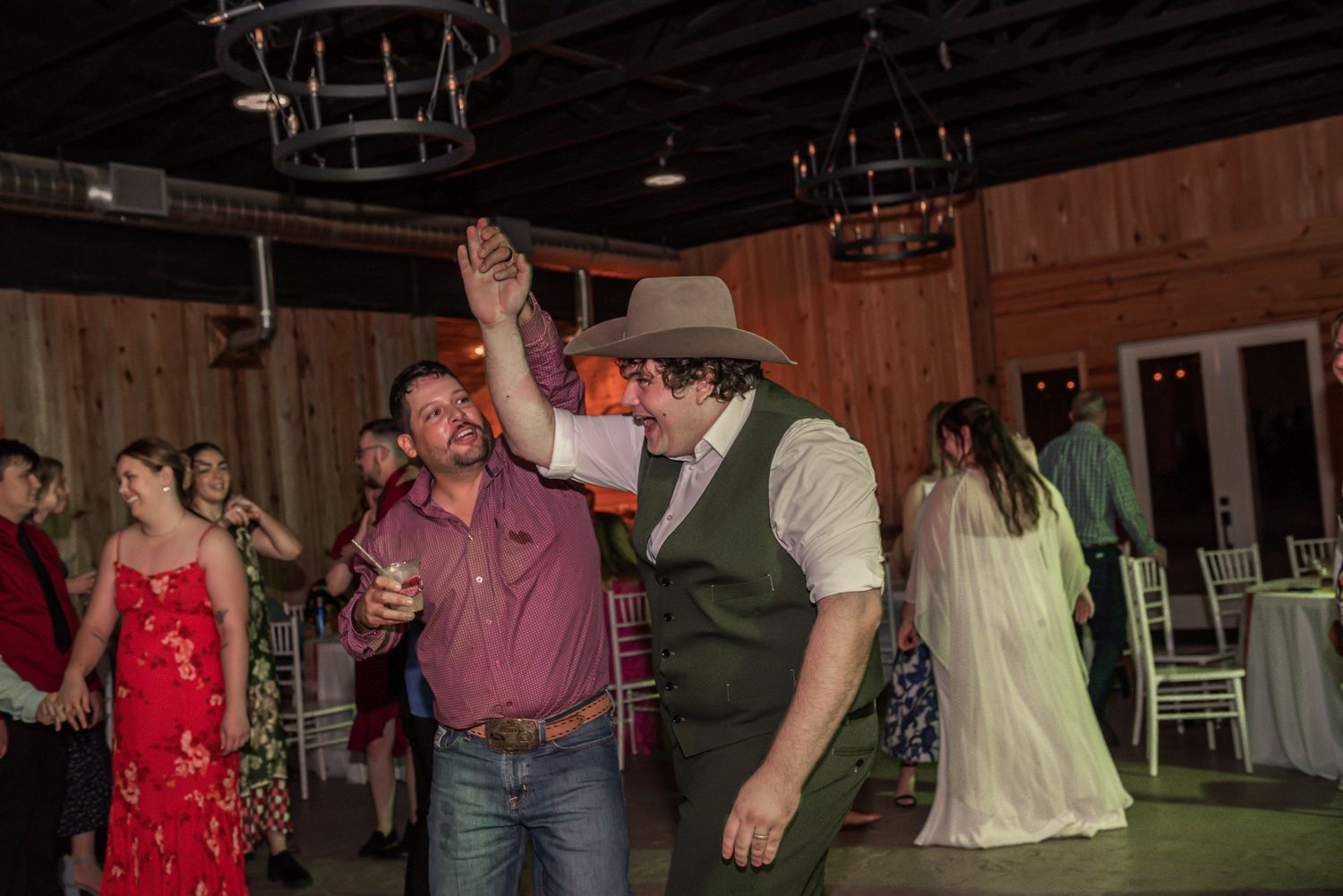 Wedding guests dancing and celebrating inside a rustic barn venue with wooden walls and festive lighting.