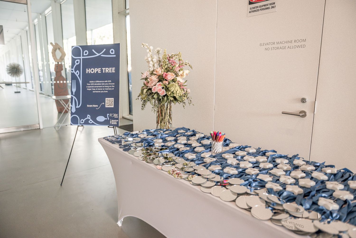 A table with blue and white party favors arranged neatly with a floral centerpiece at a corporate event.