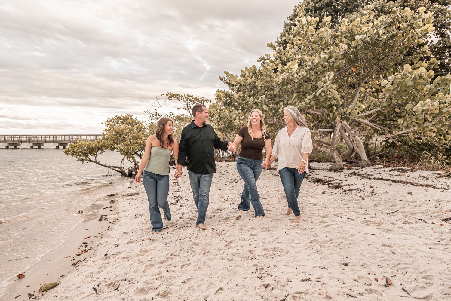 A group of people walking together on a sandy beach at sunset with trees in the background.