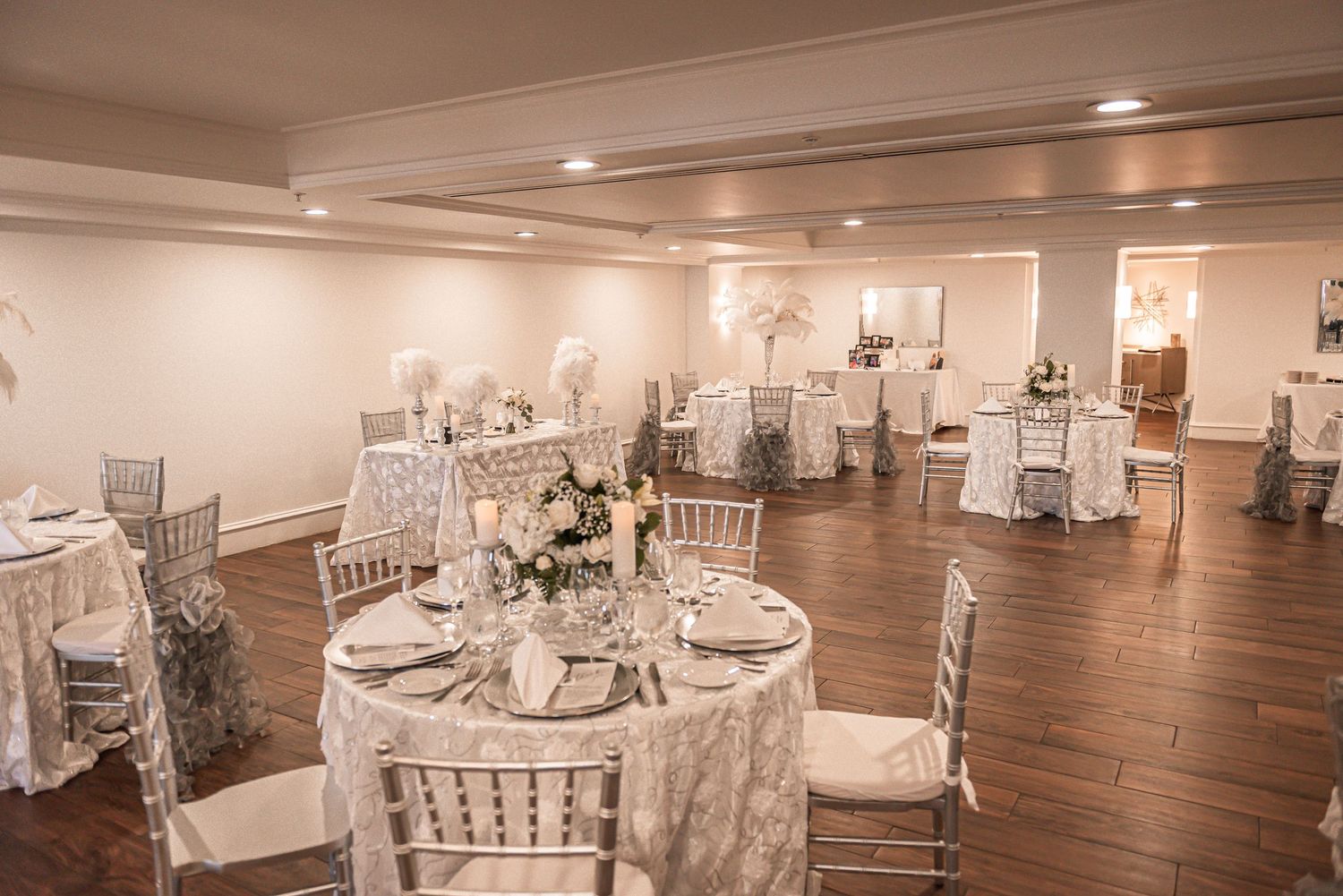 Elegant wedding reception venue with white Chiavari chairs and round tables set in a spacious banquet hall.