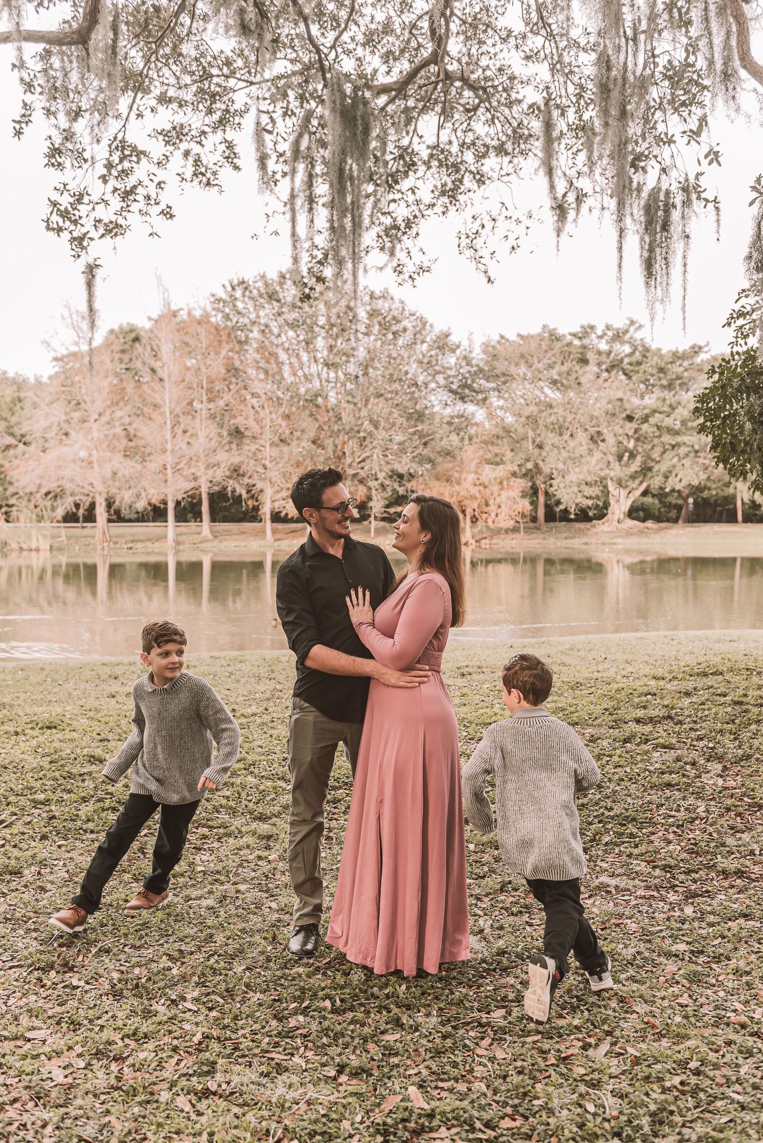 Family shares a tender moment by a lake with Spanish moss draped trees in the background during golden hour.