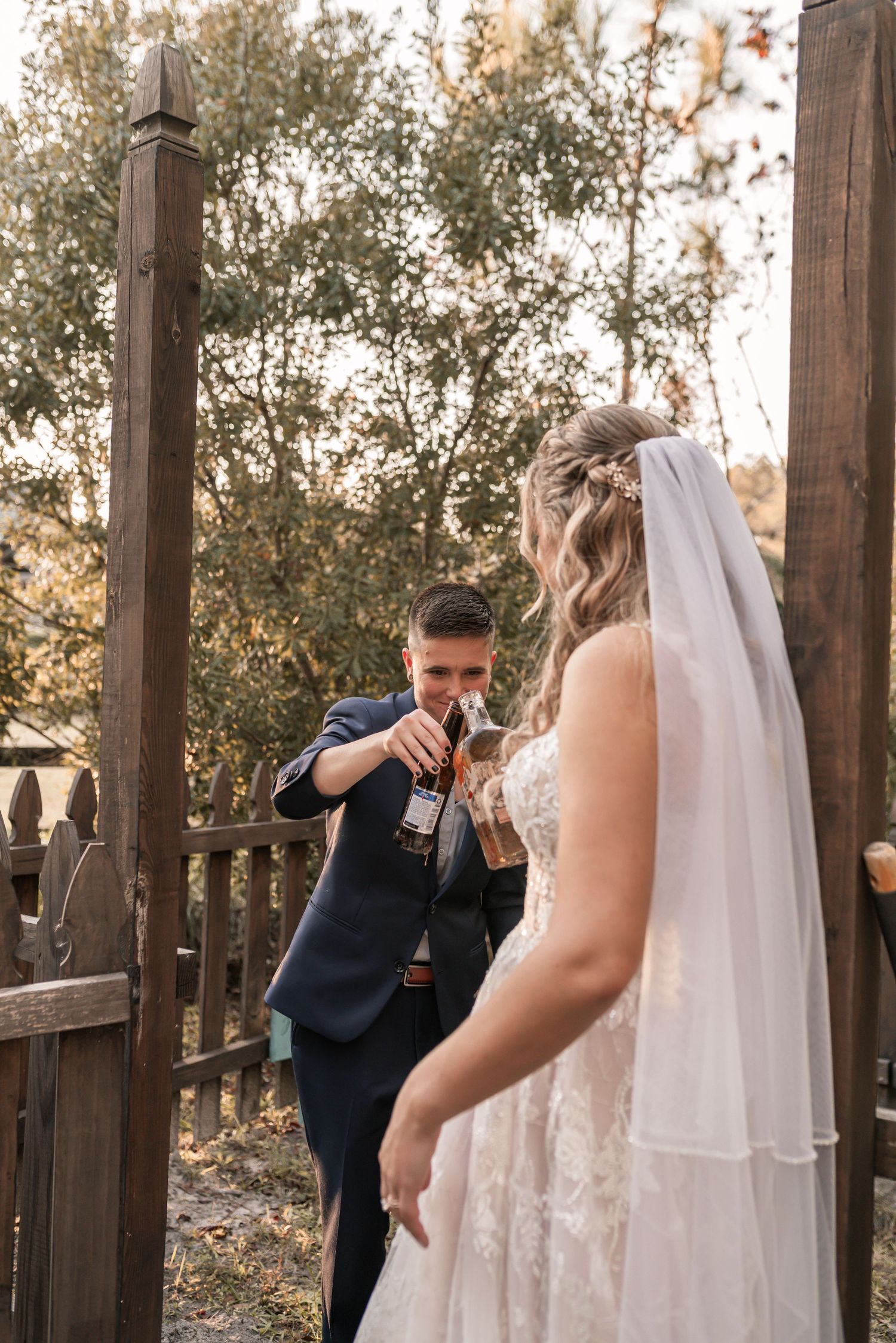 A wedding couple shares a joyful moment in an outdoor wooden gazebo during a sunset ceremony.