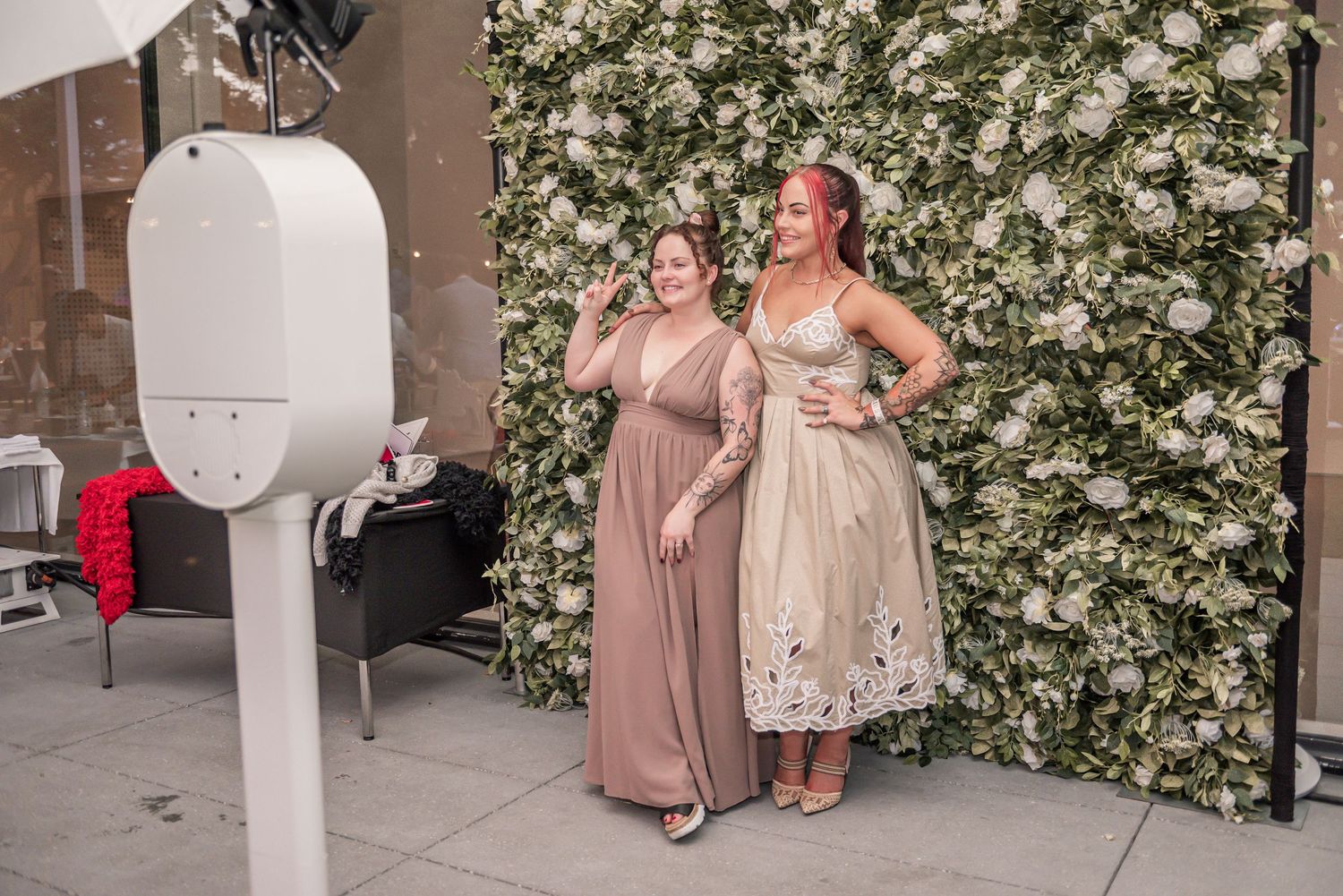 A group of bridesmaids in mauve dresses pose together in front of a floral wall at an elegant wedding venue.