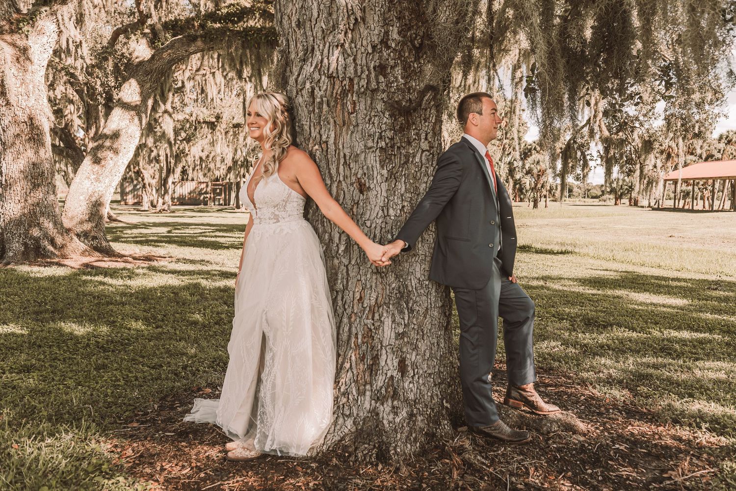 Couple in formal attire poses together under majestic oak trees in a romantic outdoor setting during golden hour.