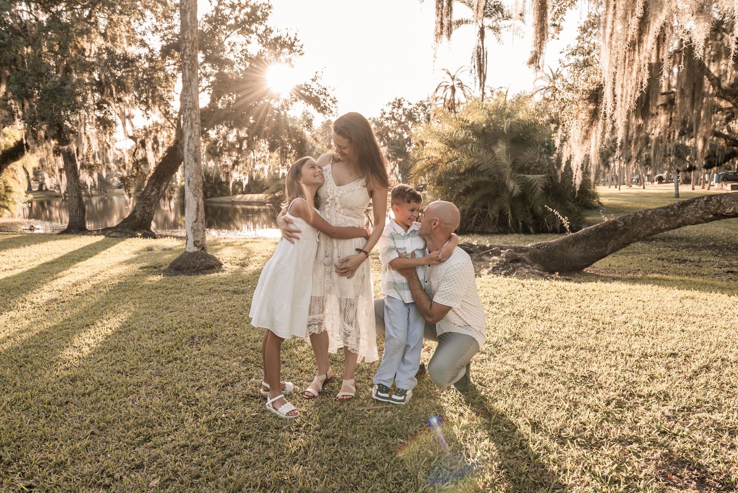 A family walks together through a sunlit park with Spanish moss hanging from oak trees during golden hour.