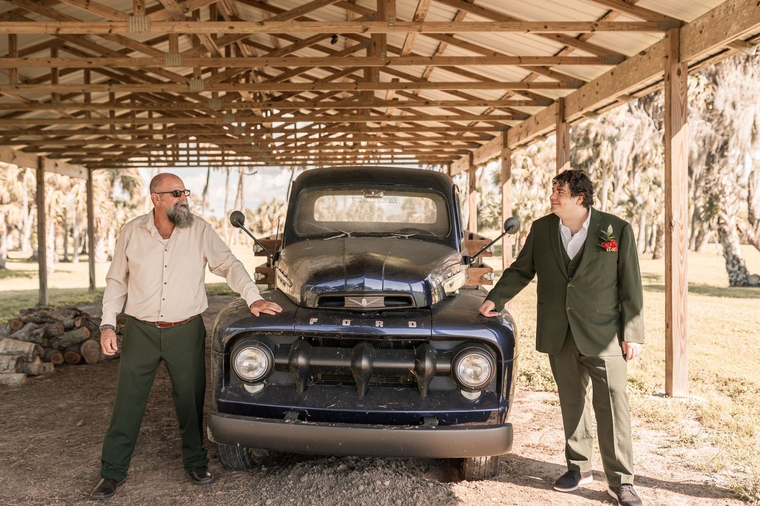 A vintage black car parked in a rustic covered area with stone pillars and wooden beams overhead.