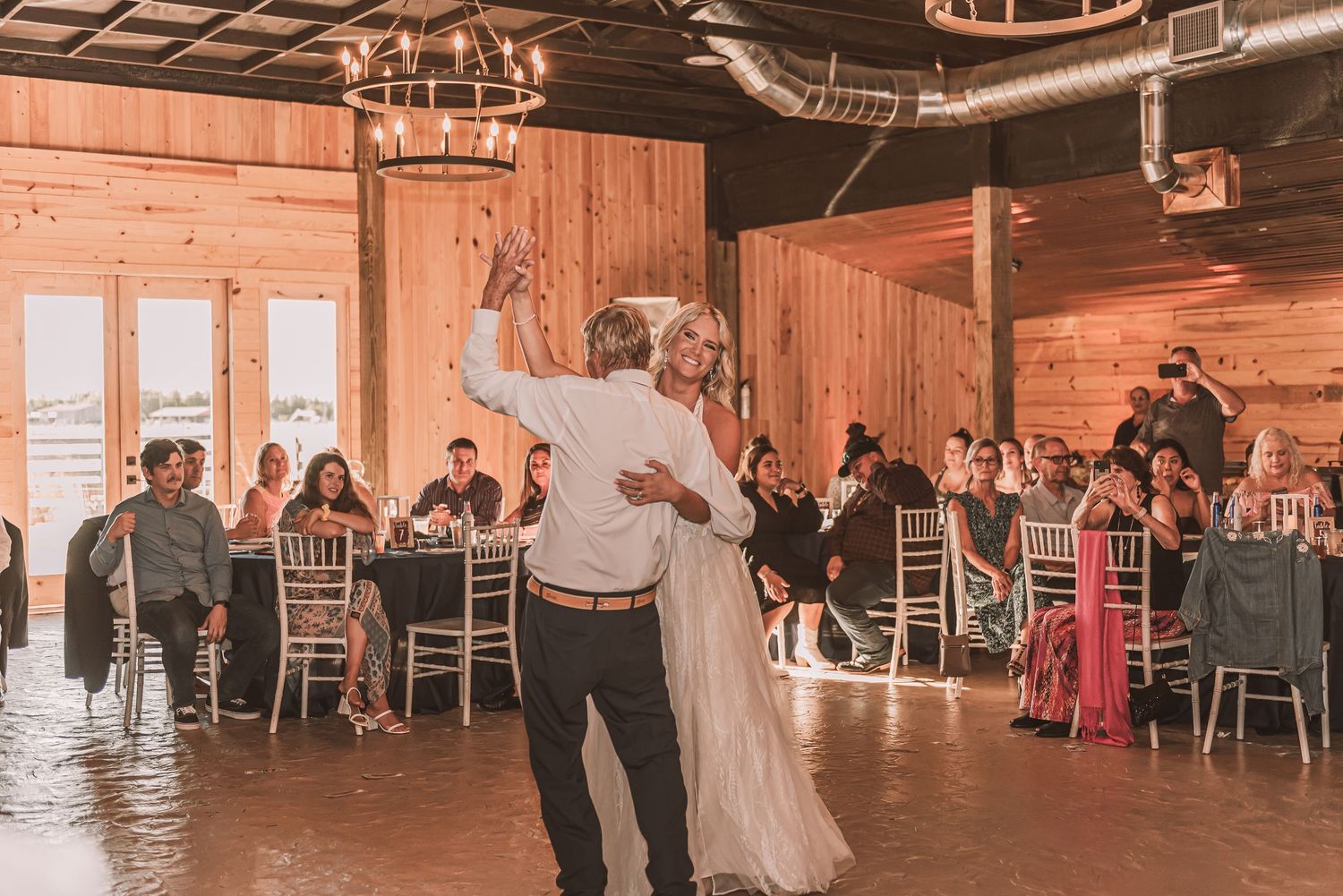 A panoramic view of a rustic wooden barn reception venue with guests seated at round tables under warm lighting.