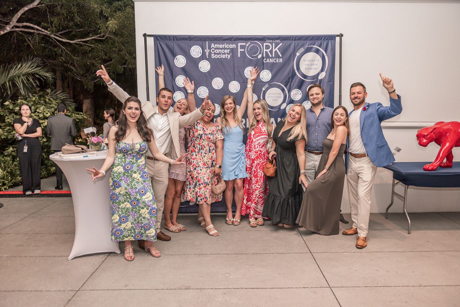 A group of people stand in a line against a white wall at a social gathering or event.
